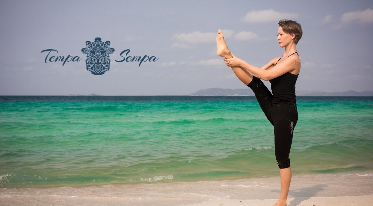 Mujuer agarrando su pierna para comenzar una clase de yoga en la playa